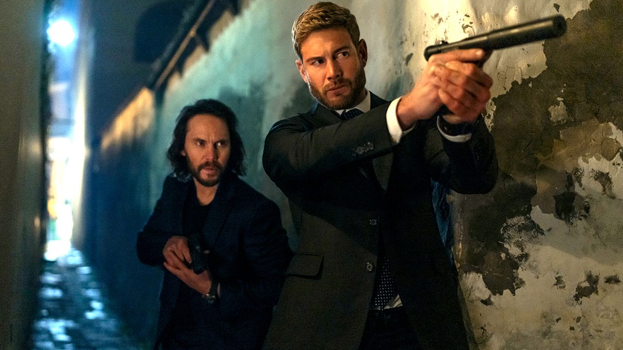 Ben, interprété par Taylor Kitsch, accroupi derrière Raife, interprété par Tom Hopper, tandis qu'ils tiennent tous les deux des armes dans The Terminal List: L'Ombre du Loup.
