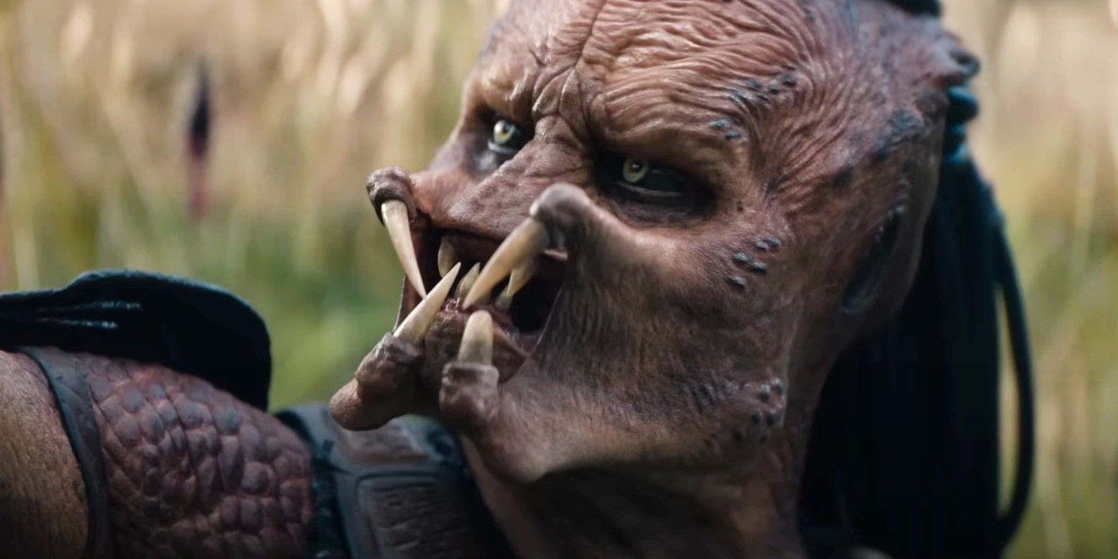 Predator: Badlands – Profil menaçant du Predator Dek, un Yautja avec ses crocs apparents et ses dreadlocks, extrait d'une séquence du film.
