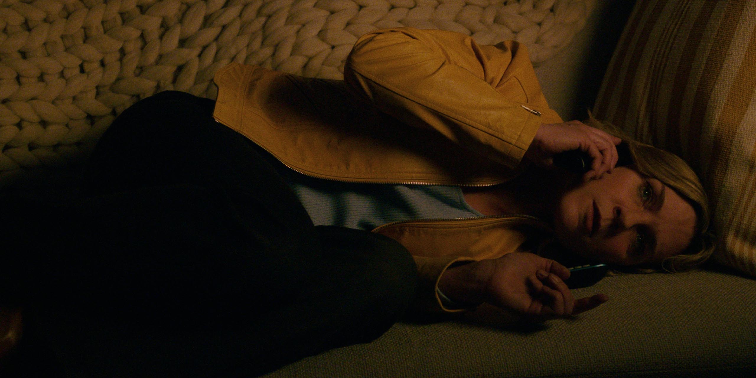 Carol (Rhea Seehorn) inquiète, au téléphone, allongée sur le canapé, dans l'épisode 1 de la saison 1 de Pluribus.