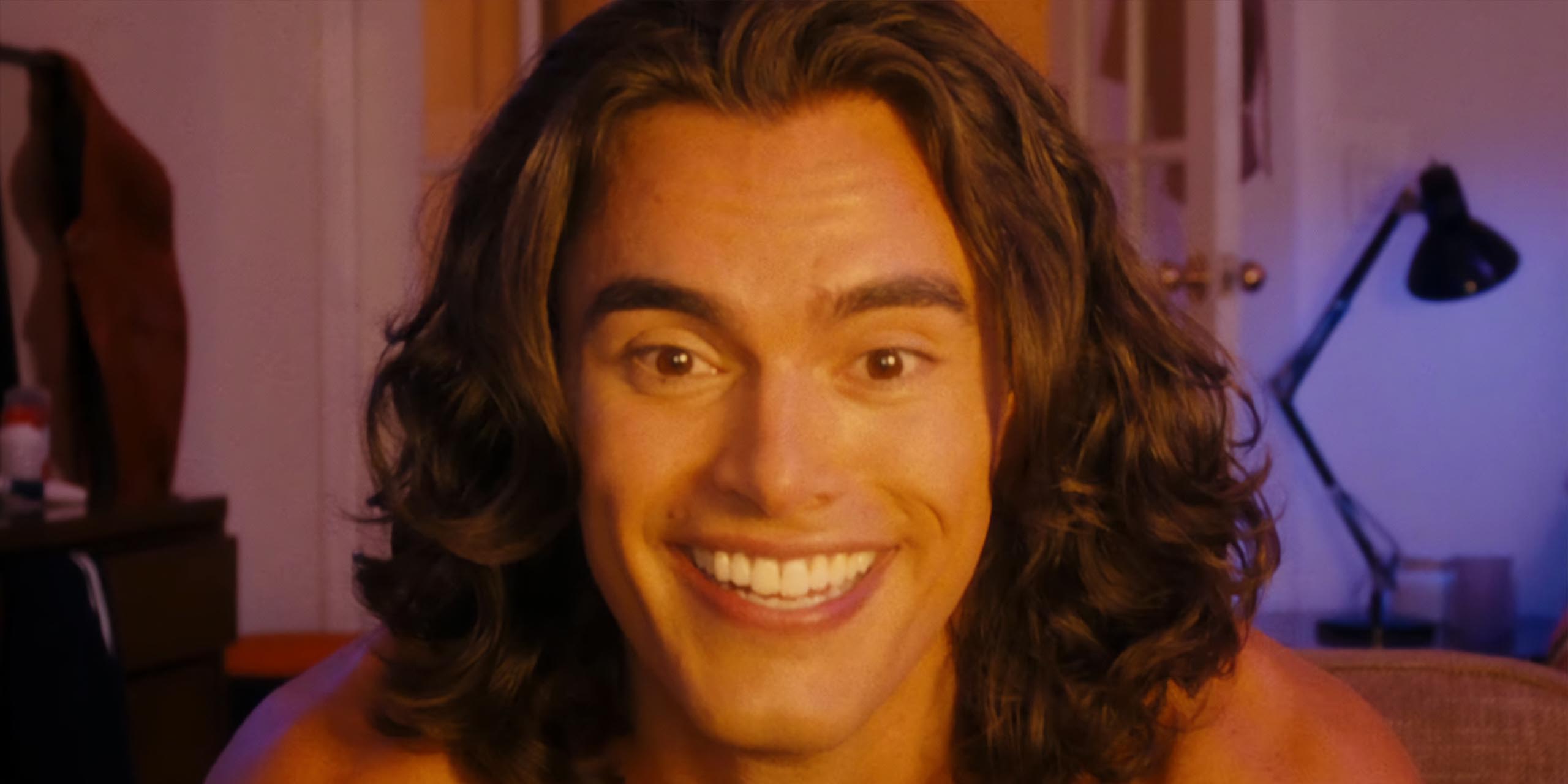 Un homme aux cheveux longs affiche un large sourire dans The Beauty.