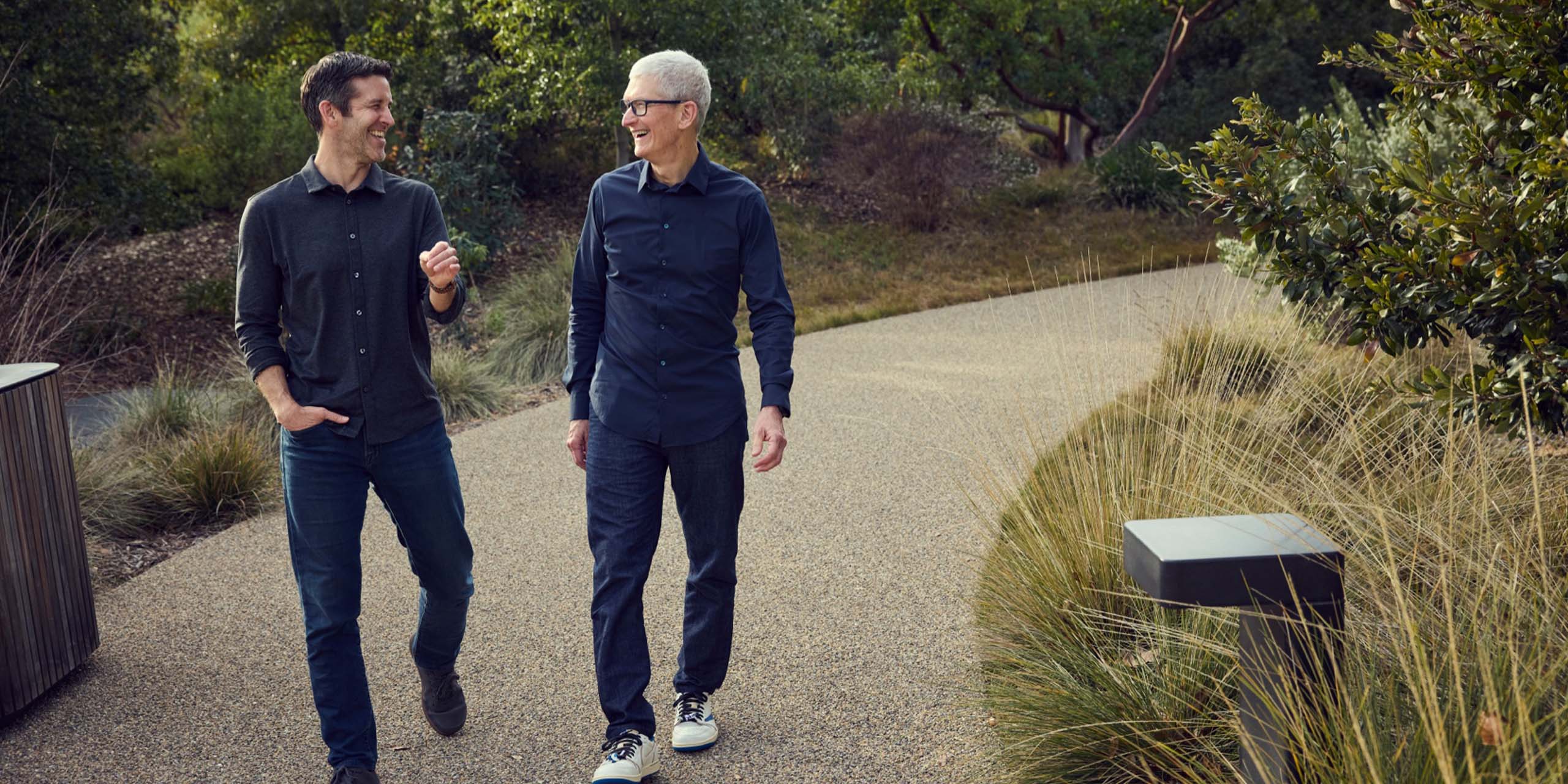 John Ternus et Tim Cook, les dirigeants d'Apple, marchant en riant dans un parc.