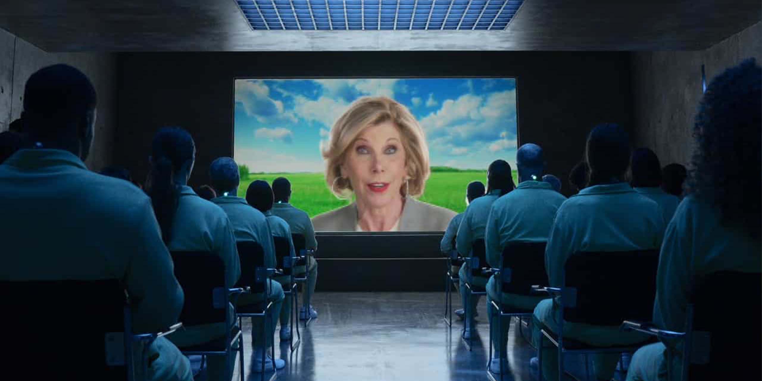 Christine Baranski présente une vidéo de propagande sur un écran face à une salle pleine de prisonniers dans la saison 1 de Stuart Fails to Save the Universe