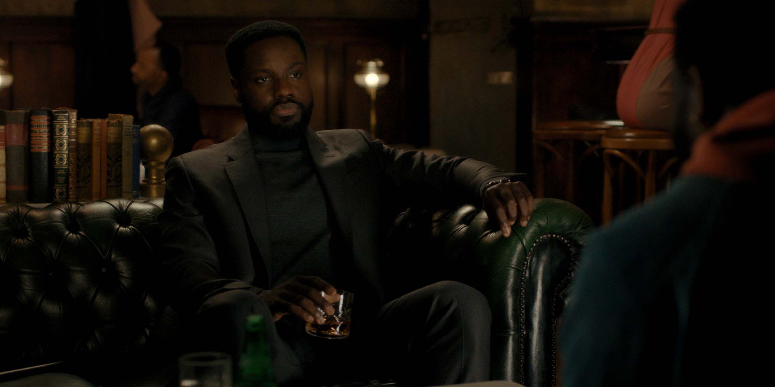 Leighton Vance (Dayo Okeniyi) buvant un whisky assis sur un fauteuil dans la saison 2 de Dark Matter.