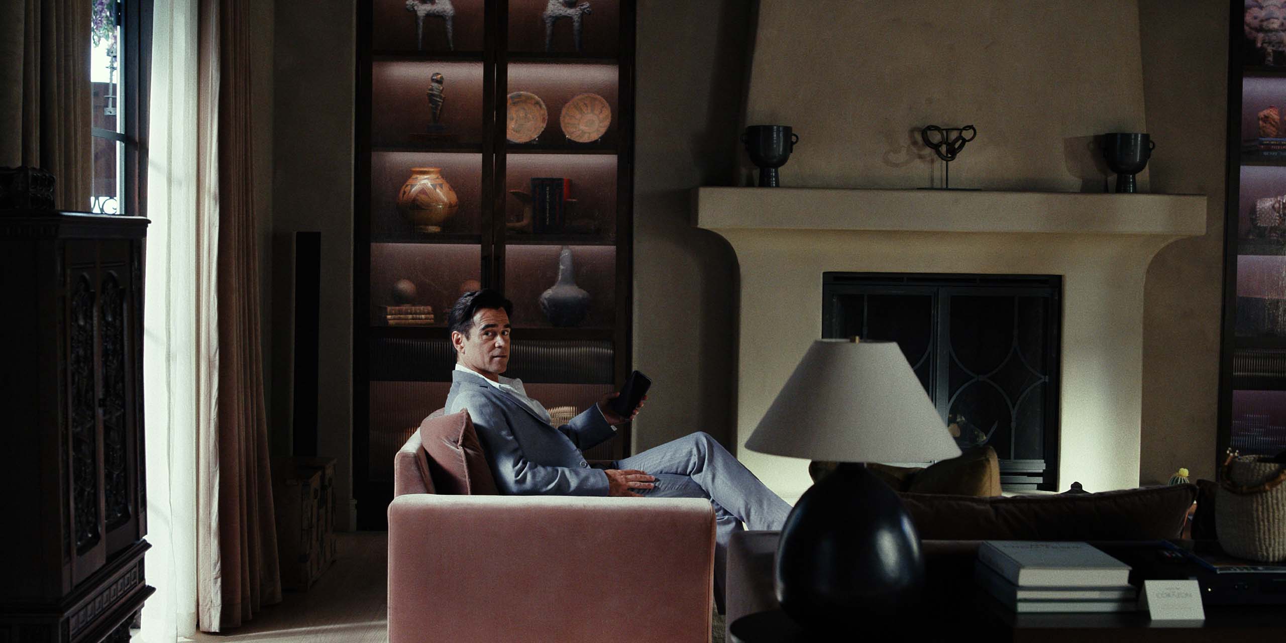 John (Colin Farrell) assis sur un canapé, une télécommande à la main, dans la saison 2 de Sugar.