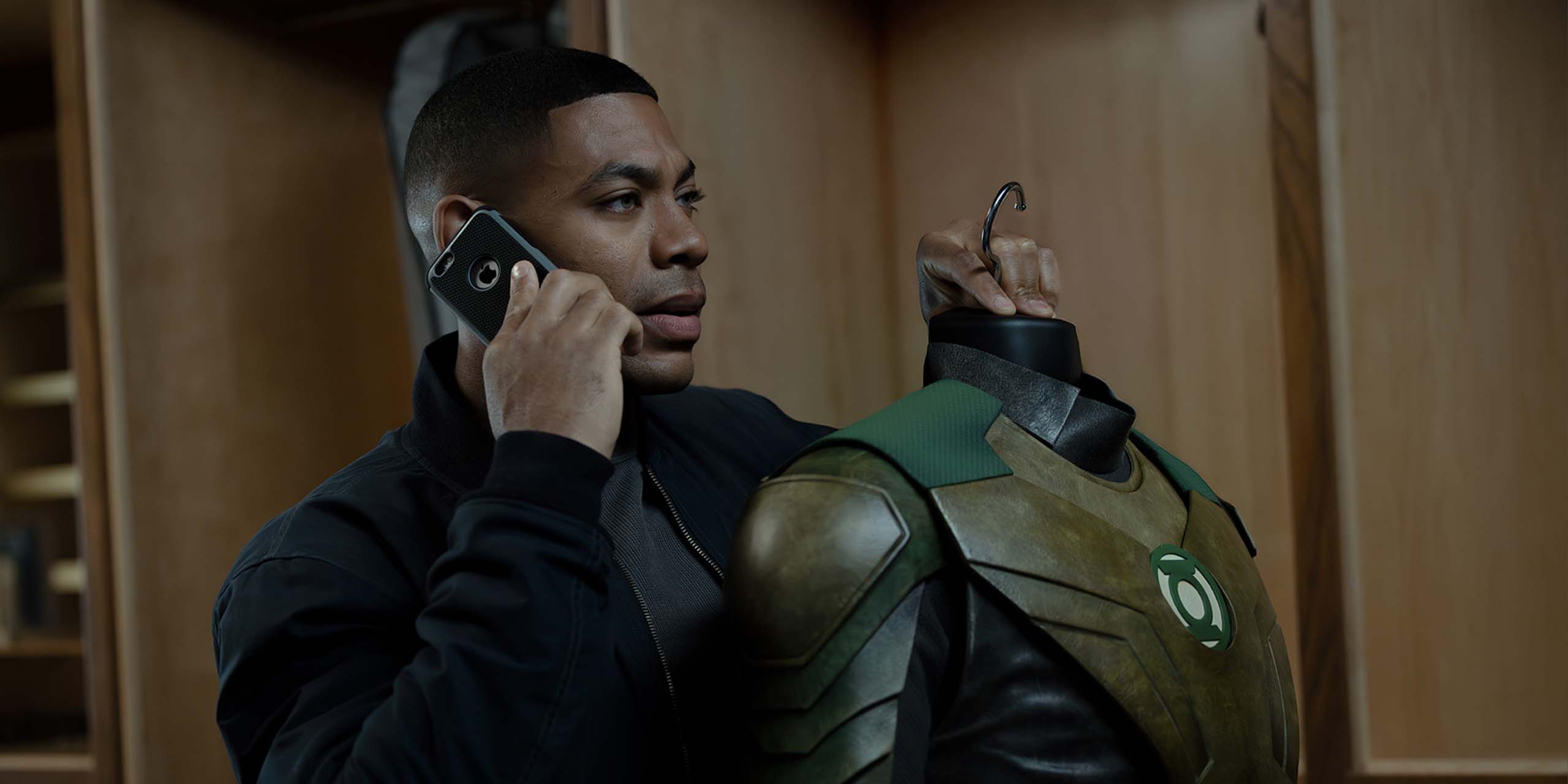 John Stewart (Aaron Pierre) au téléphone, observant un costume de Green Lantern dans la série Lanterns.
