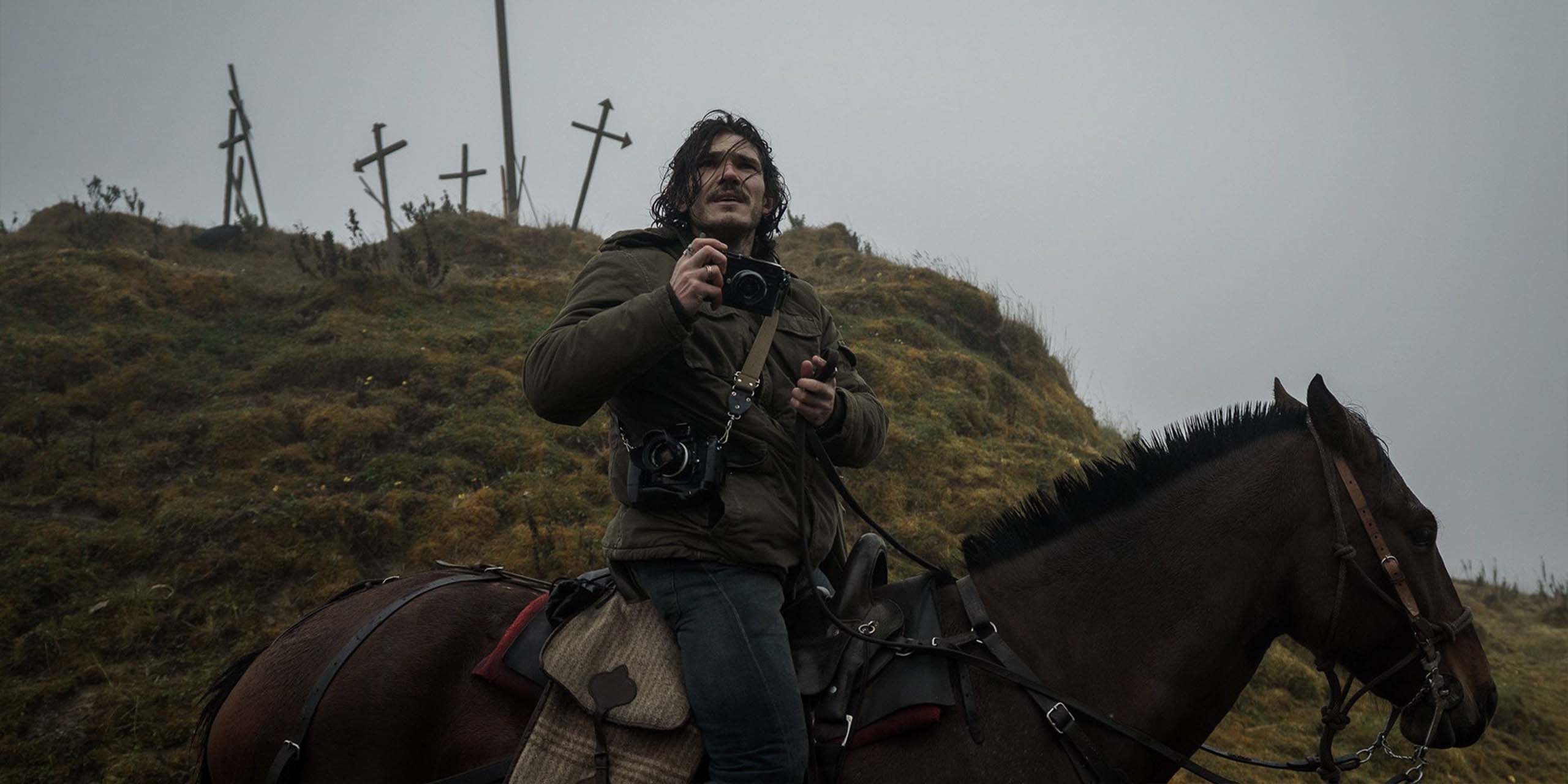 Un photographe à cheval dans un paysage brumeux de « The Last Photograph », avec plusieurs croix dressées sur la colline.