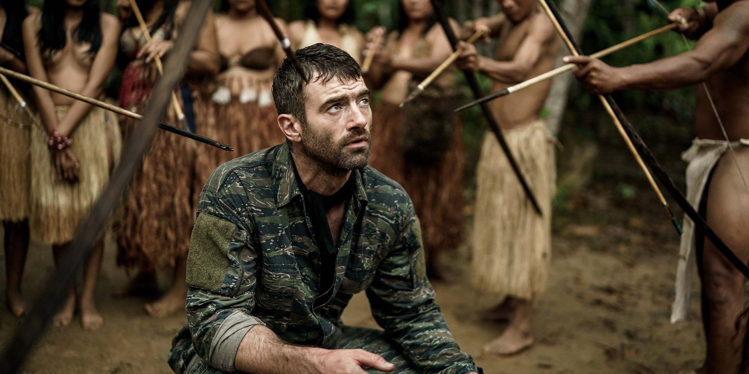 Un homme à genoux encerclé par plusieurs personnes armées d’arcs et de flèches dans « The Last Photograph ».