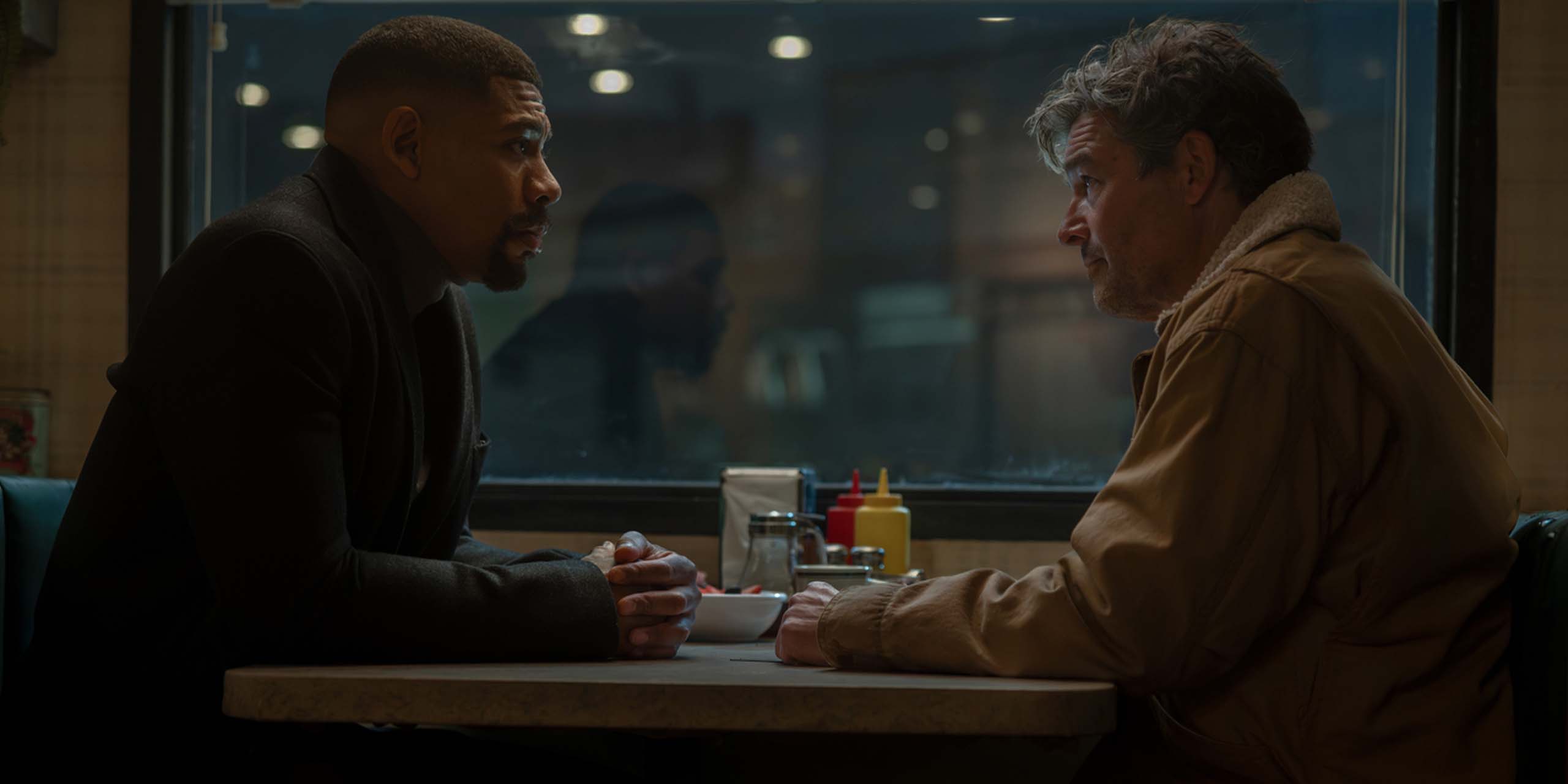 John Stewart (Aaron Pierre) et Hal Jordan (Kyle Chandler) à la table d'un restaurant à Rushville en 2026 dans Lanterns.