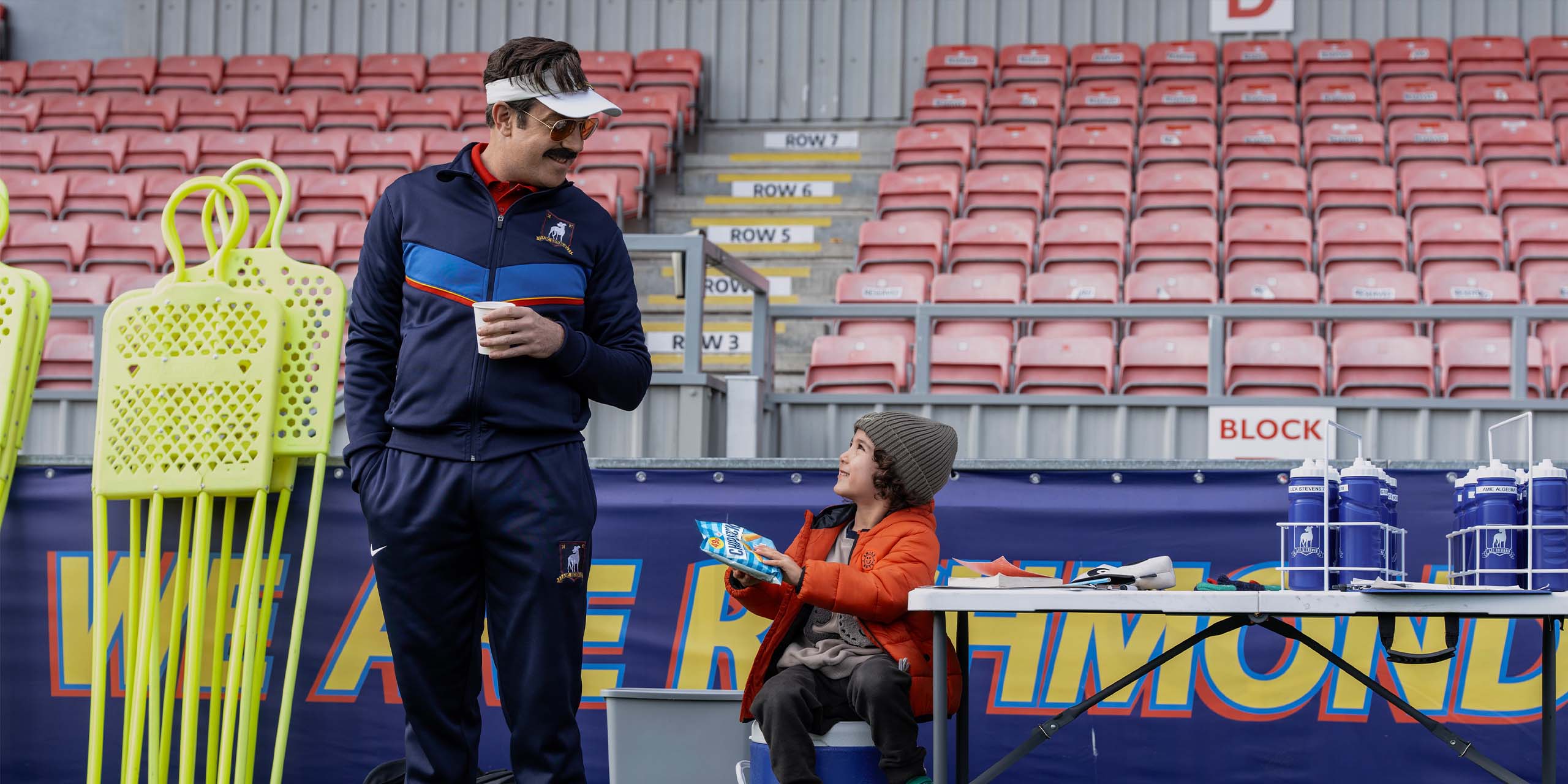 Ted (Jason Sudeikis) discutant avec le fils de Lizzie (Faye Marsay) durant l'entraînement dans la saison 4 de Ted Lasso.