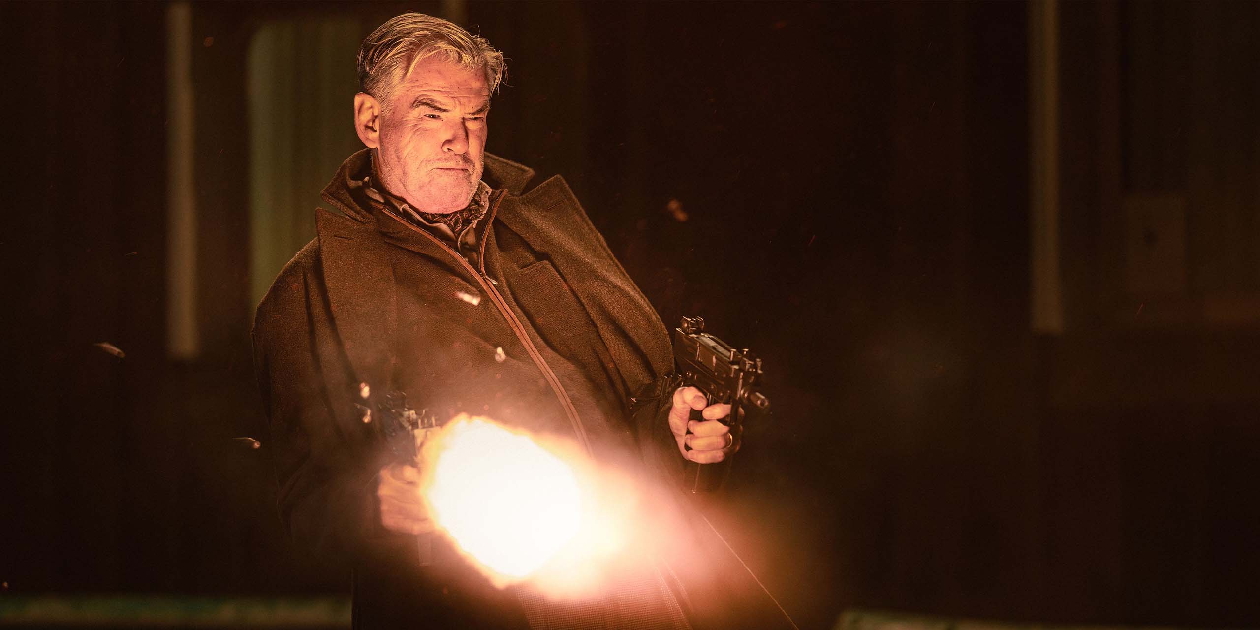 Pierce Brosnan dans le rôle de Conrad Harrigan tirant avec deux Uzis dans la saison 2 de MobLand.