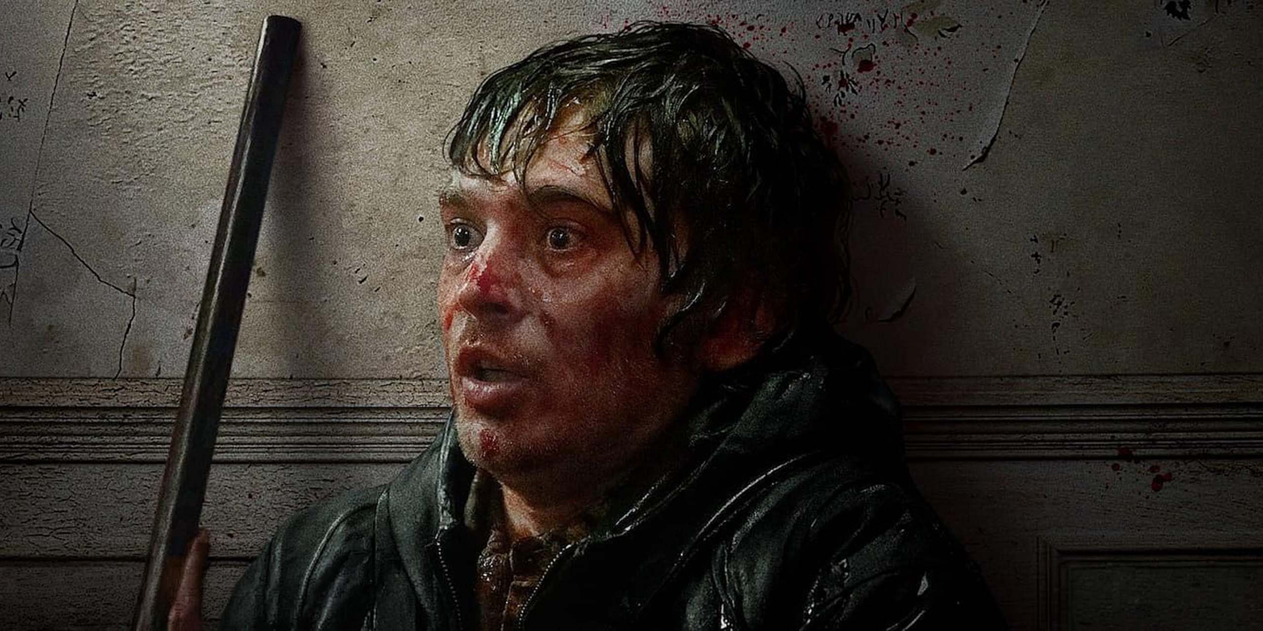 Bryan (Austin Abrams) blessé, adossé contre un mur à côté de son fusil dans le film Resident Evil (2026).
