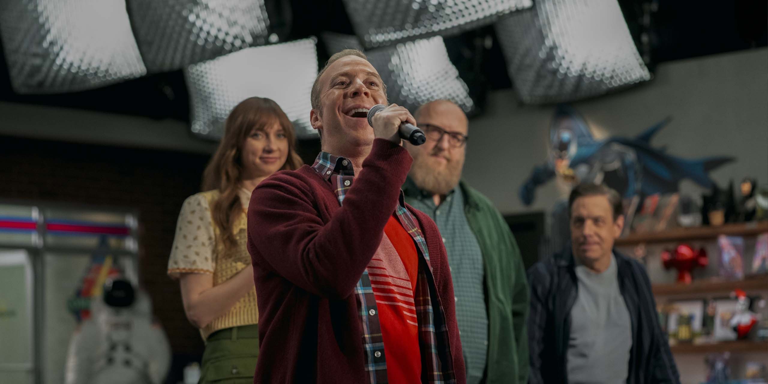 Stuart Bloom (Kevin Sussman) s'adressant au public avec un micro, accompagné de Denise (Lauren Lapkus), Bert Kibbler (Brian Posehn) et Barry Kripke (John Ross Bowie) dans le final de Stuart fails to save the universe.
