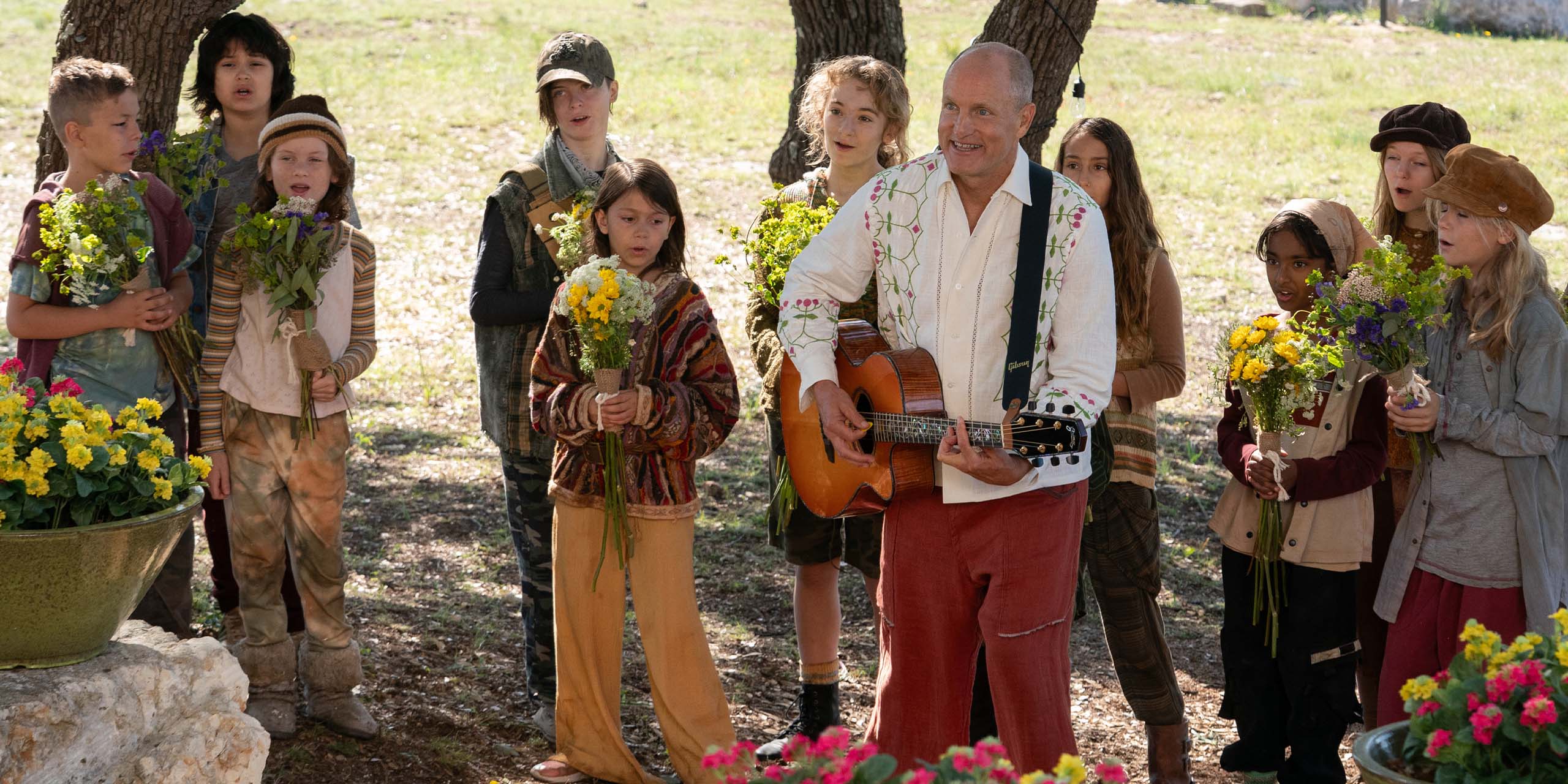Woody Harrelson et joue de la guitare entouré d'enfants dans Brothers.