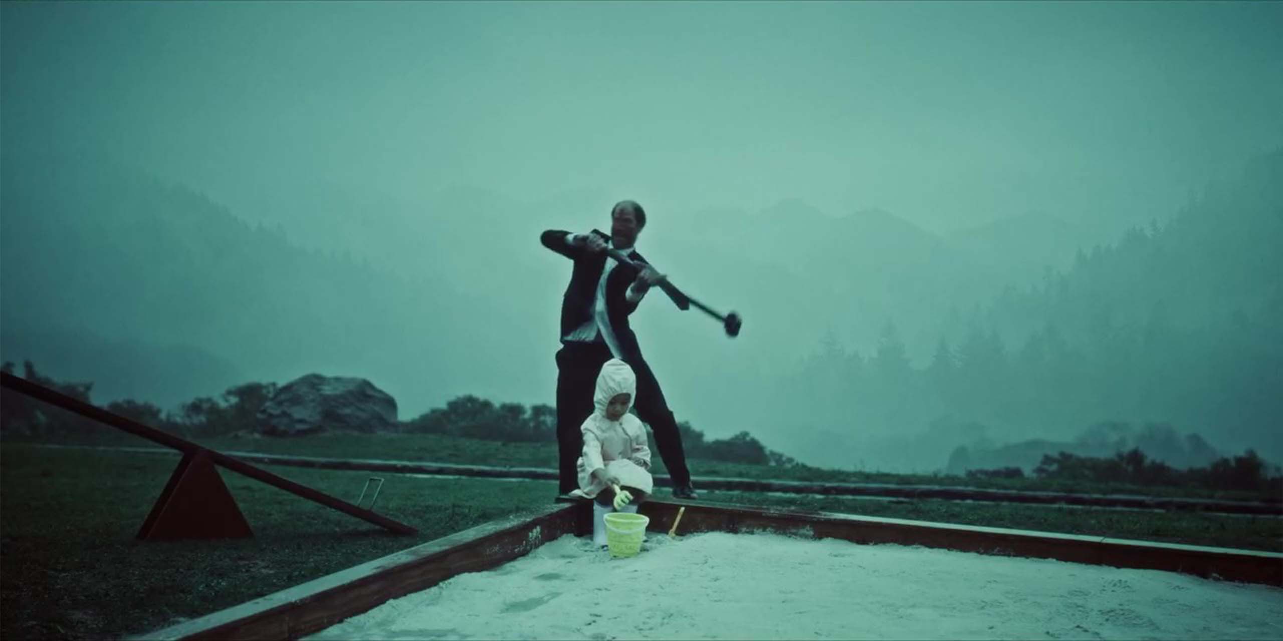 Un infecté tenant une masse devant un enfant qui joue dans un bac à sable, dans le film Crossed (2026).