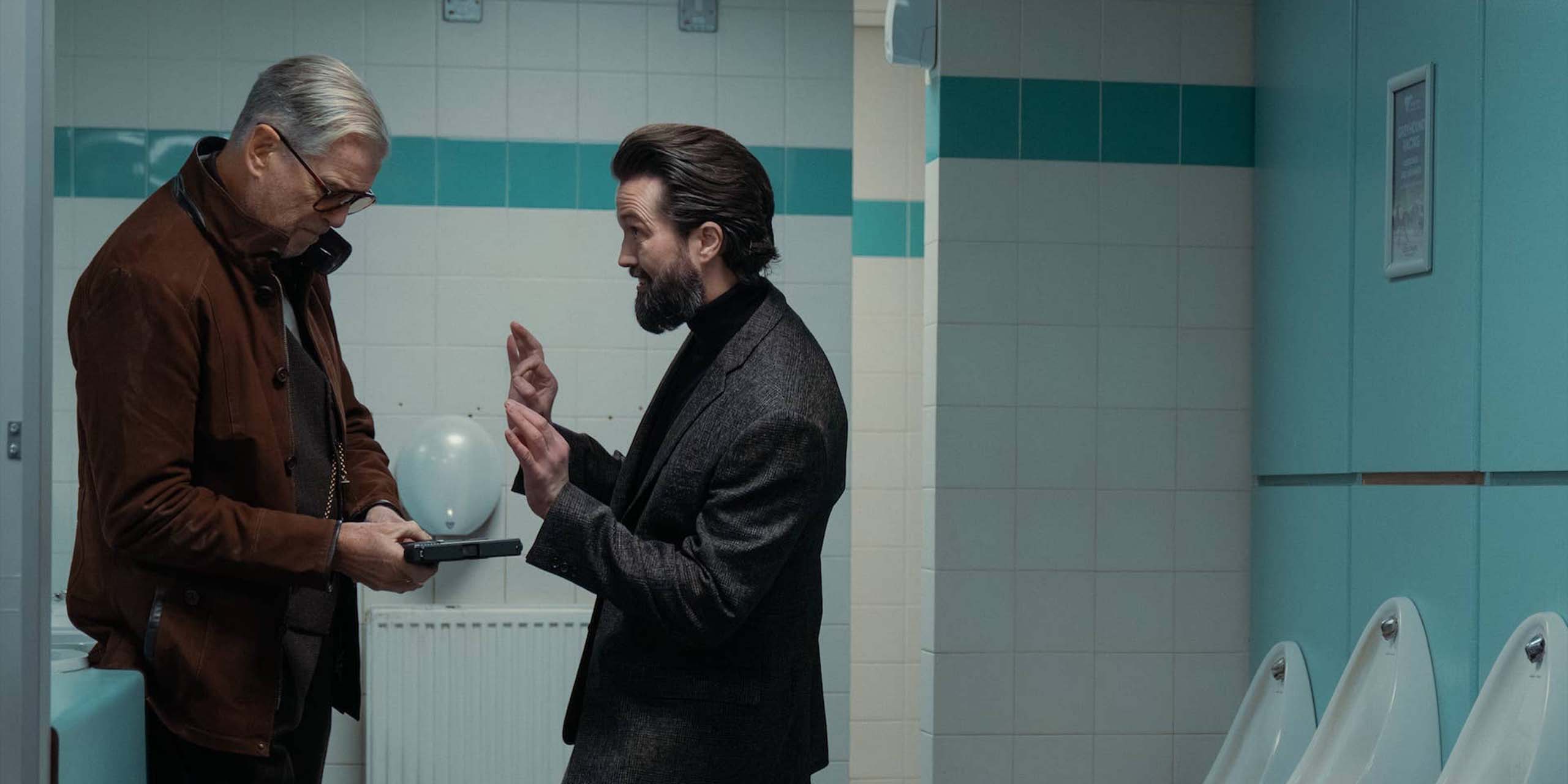 Conrad Harrigan (Pierce Brosnan) et Emmett J. Scanlan (Paul) dans les WC dans MobLand, épisode 2, saison 2
